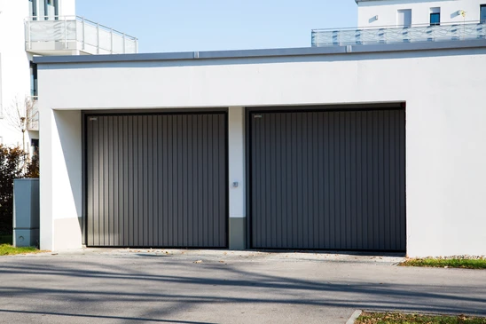 Garage moderne à deux portes sectionnelles coulissantes en lamelles métalliques anthracite intégrées dans façade contemporaine blanche