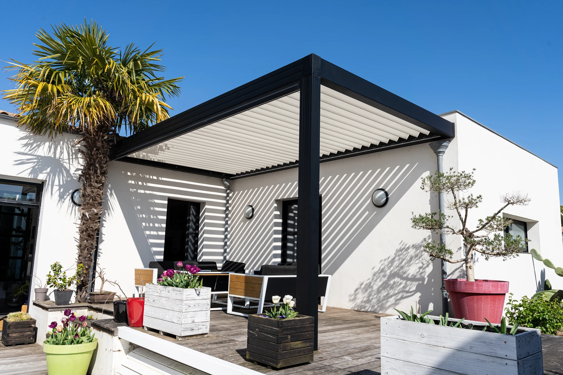 Scène extérieure de jardin avec pergola moderne abritant un salon de jardin en résine tressée marron