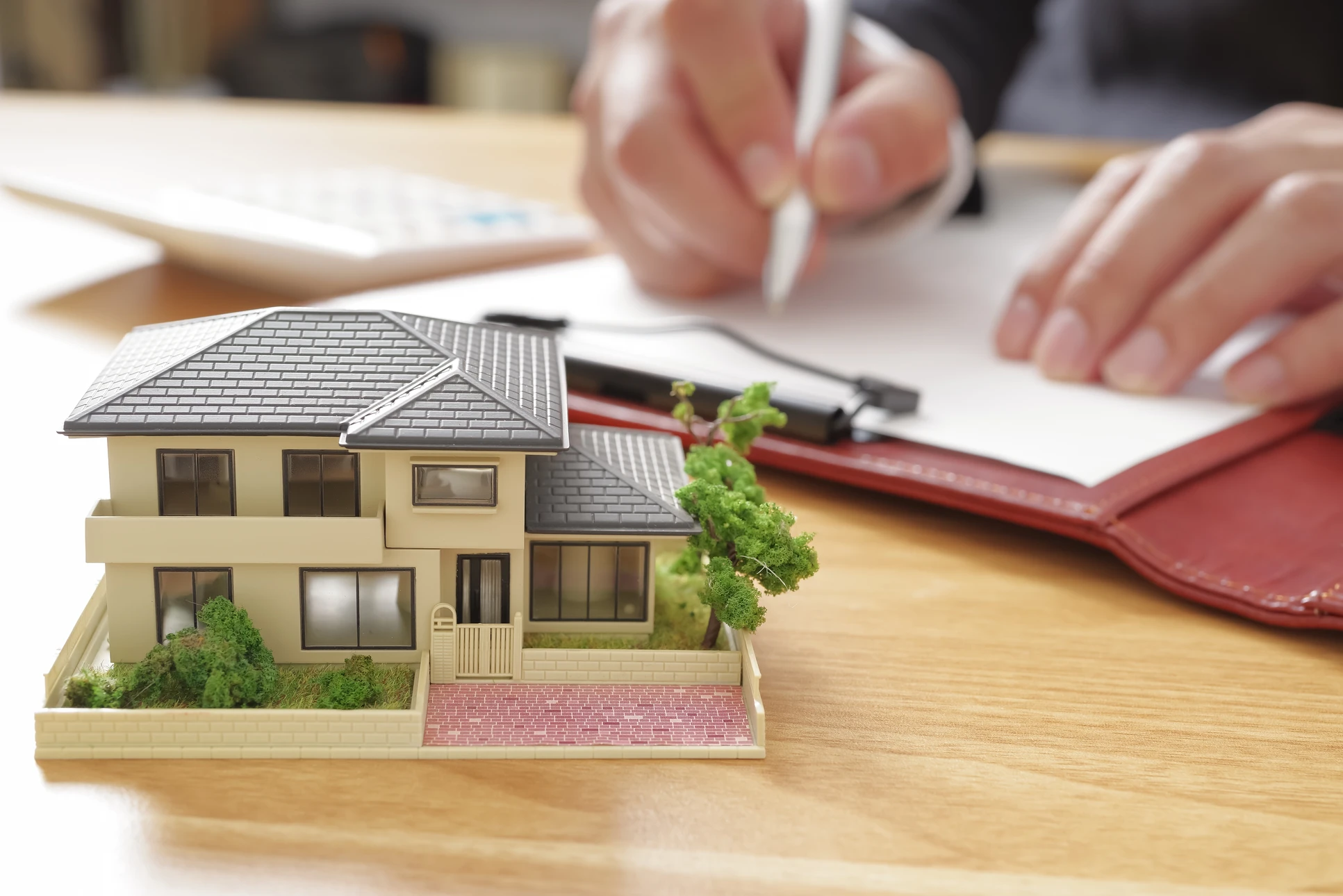 Main de professionnel tenant une loupe devant une villa moderne contemporaine avec terrasse dallée, façade mixte brique et verre, baies vitrées coulissantes et espaces verts paysagers