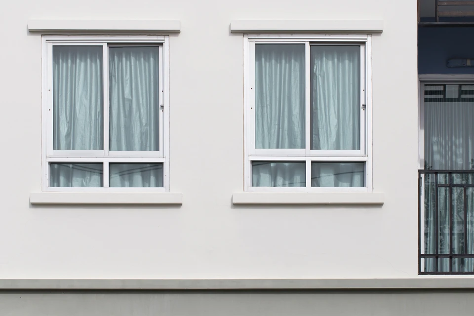 Façade de maison résidentielle avec volets blancs ouverts, fenêtres à petits carreaux et garde-corps métalliques