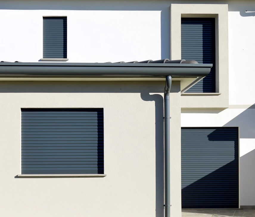 Façade de maison traditionnelle française aux murs blancs avec volets bleus ouverts, porte-fenêtre centrale et fenêtres à l'étage